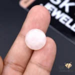Round rose quartz gemstone held between fingers, showcasing its translucent pink color and smooth surface