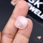 Hand holding a 13.45-carat natural rose quartz gemstone between thumb and index finger, showcasing its transparent pink color