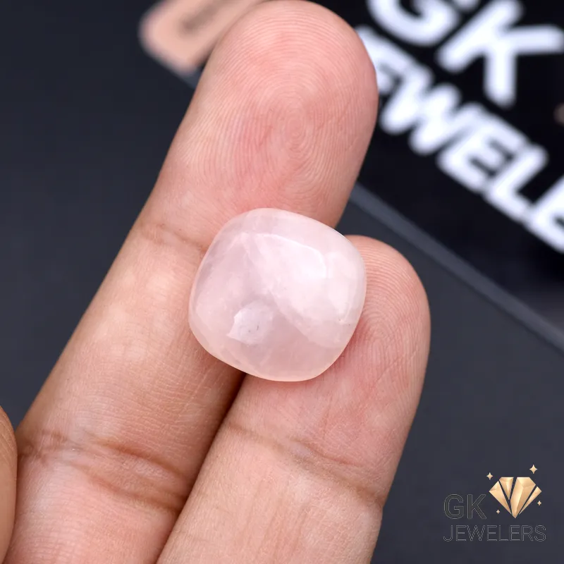 Hand holding a 13.45-carat natural rose quartz gemstone between thumb and index finger, showcasing its transparent pink color