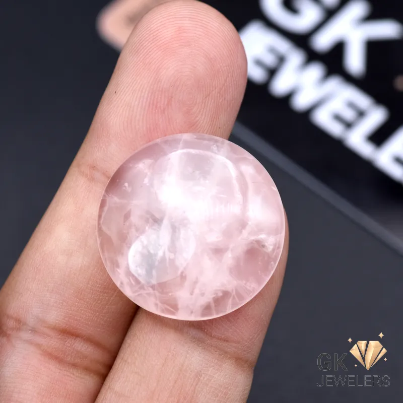 Hand holding a round, semi-transparent pink rose quartz gemstone with visible inclusions