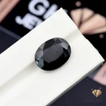 Oval-cut black tourmaline gemstone on a white display stand, showcasing its opaque texture and deep coloration