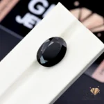 Oval-cut black tourmaline gemstone on white textured surface, weighing 10.80 carats, from Afghanistan