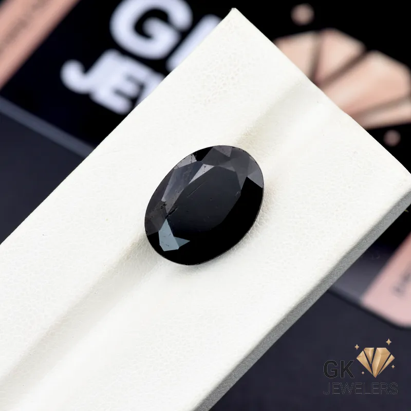 Oval-cut black tourmaline gemstone on white textured surface, weighing 10.80 carats, from Afghanistan