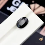 Opaque black tourmaline gemstone with faceted oval cut on white display stand