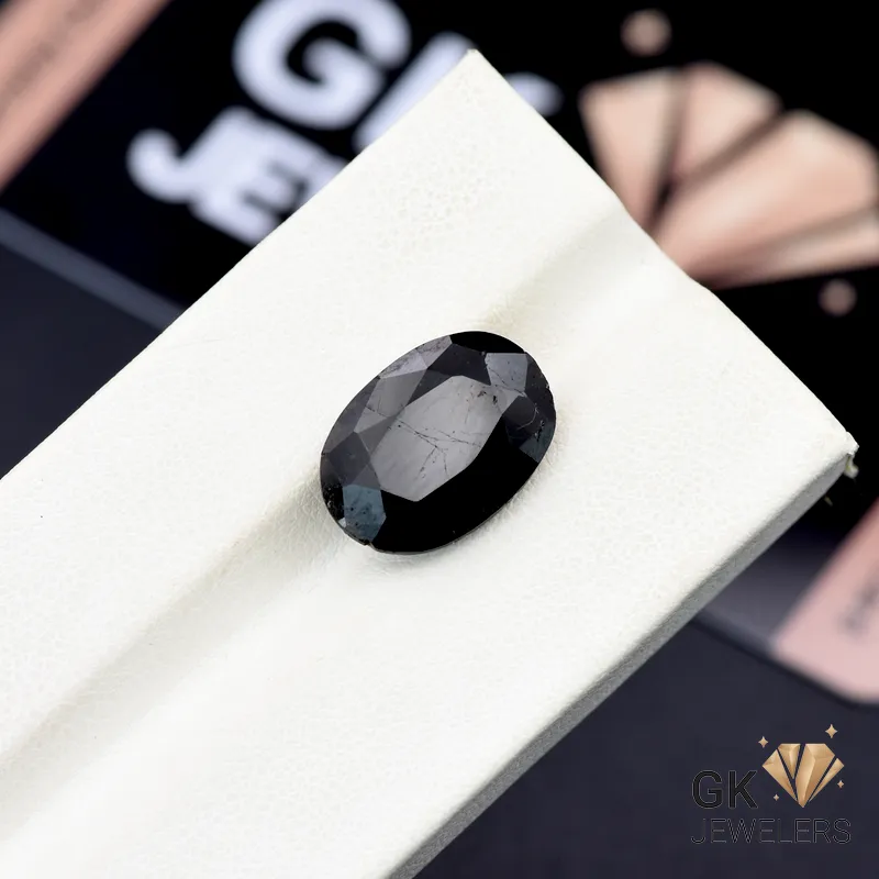 Opaque black tourmaline gemstone with faceted oval cut on white display stand