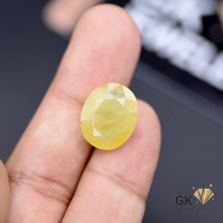 Hand holding an oval-cut yellow sapphire gemstone with semi-transparent clarity