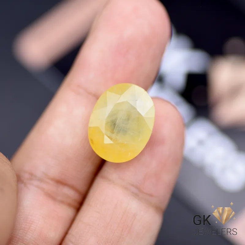 Finger holding a 19.29-carat oval-cut yellow sapphire gemstone with semi-transparent clarity