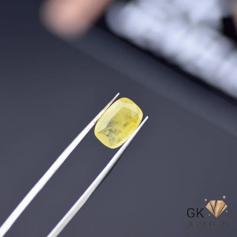 Cushion-cut yellow sapphire gemstone held by tweezers on a dark grey surface, showcasing semi-transparency and vibrant color