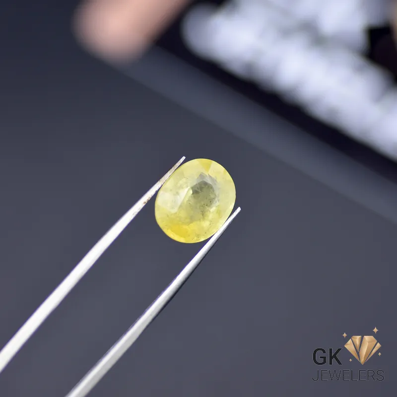 Oval-cut 5.18ct yellow sapphire gemstone held by tweezers, showcasing semi-transparent golden-yellow color