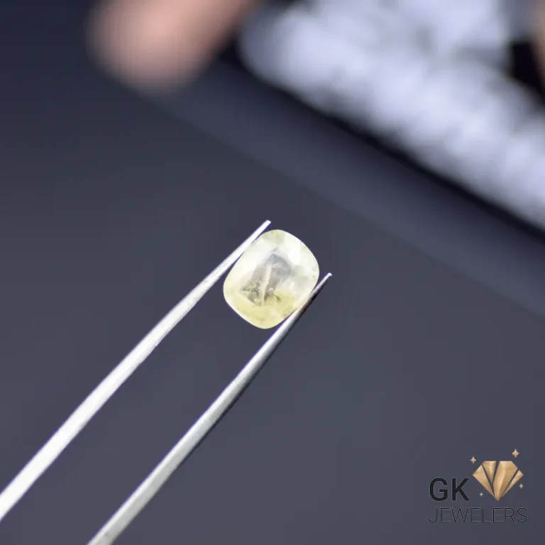 Cushion-cut yellow sapphire gemstone held by silver tweezers, showcasing semi-transparent clarity on a dark background
