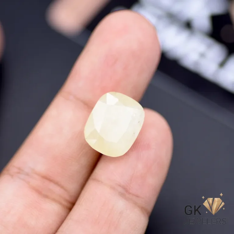 Cushion-cut yellow sapphire gemstone held between person's fingers, showcasing its translucent properties and 14.60-carat weight