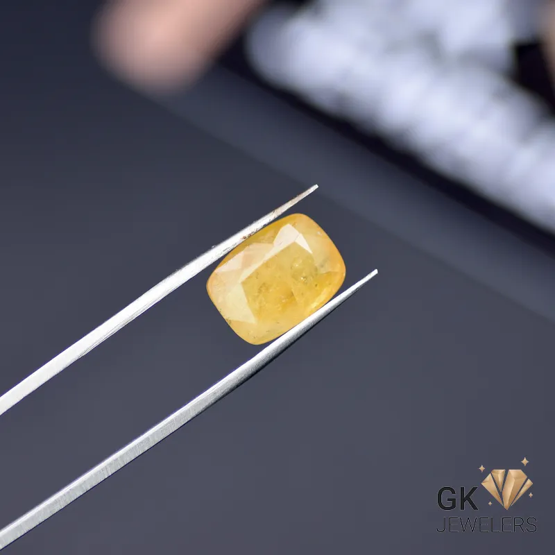 Oval yellow sapphire gemstone held by tweezers, showcasing semi-transparent clarity and golden tones