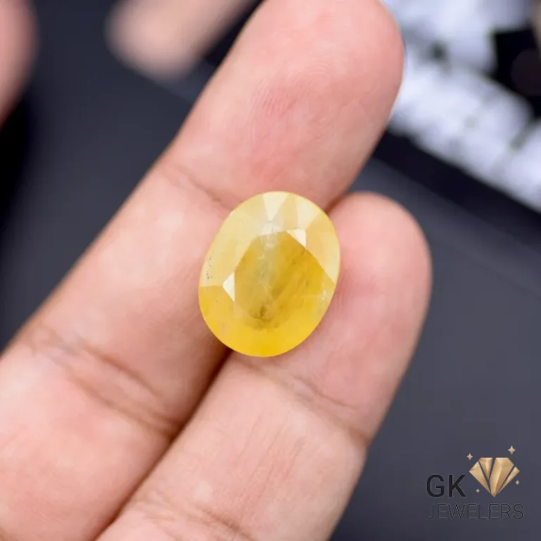 Oval-cut yellow sapphire gemstone weighing 16.34 carats, held between fingers, showcasing semi-transparent clarity and vibrant golden color
