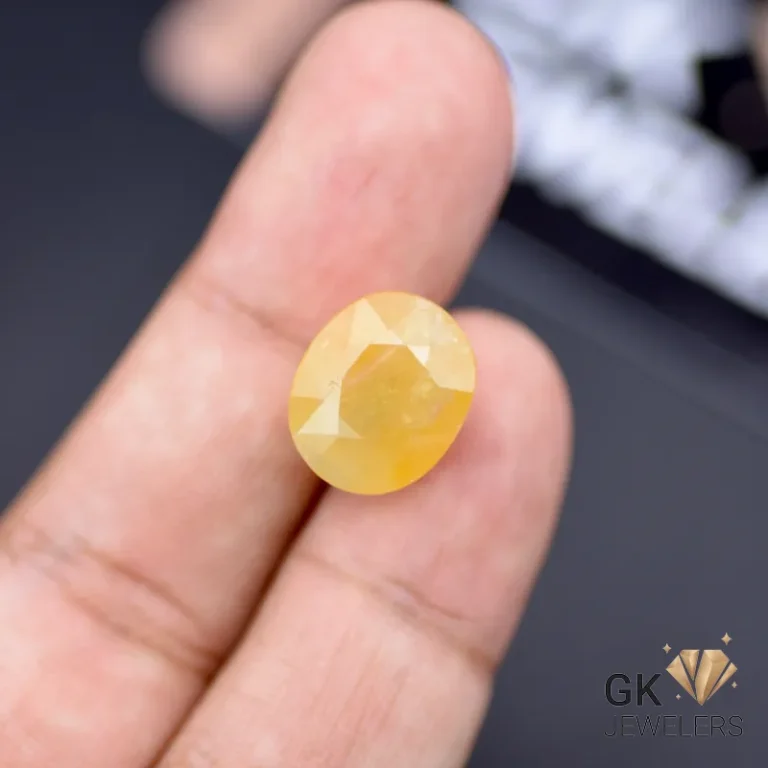 Oval-cut 15.17ct yellow sapphire gemstone held between fingers, showcasing semi-transparent clarity and golden glow
