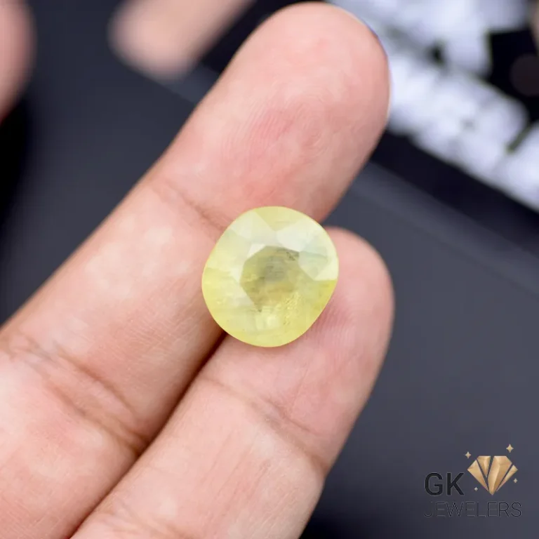 Oval-cut yellow sapphire gemstone held between fingers, showcasing its semi-transparent quality and warm golden radiance
