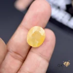 Oval-cut 14.47ct yellow sapphire gemstone held between fingers, showcasing semi-transparent golden tones