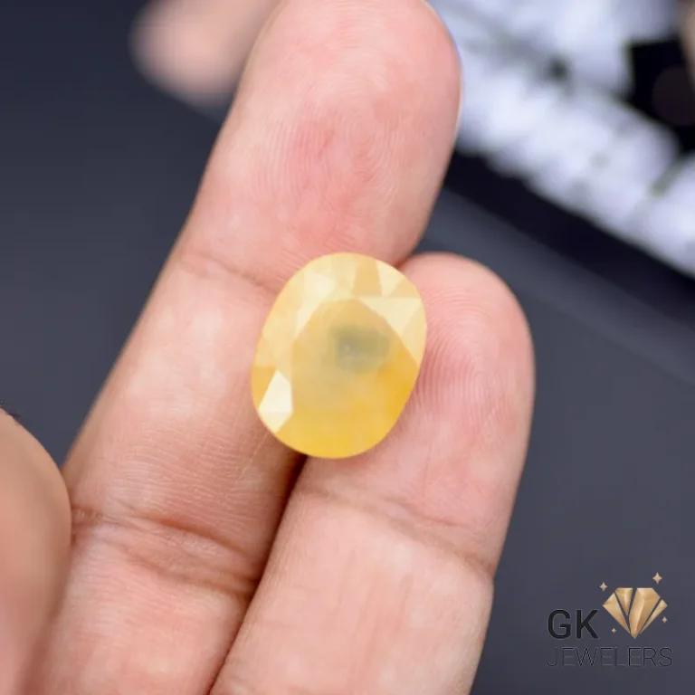Hand holding a 14.71-carat oval yellow sapphire gemstone with semi-transparent clarity
