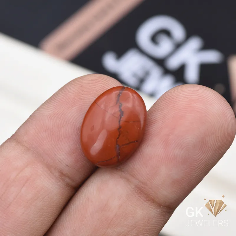 Oval red jasper gemstone with dark veining held between fingers