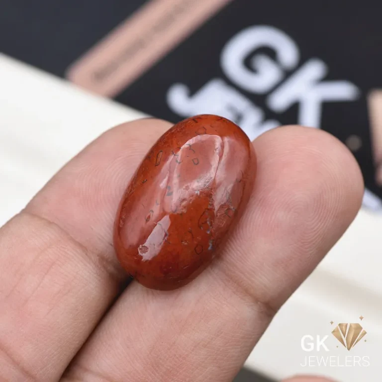 Fingers holding polished red oval gemstone with dark inclusions