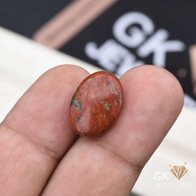 Red oval jasper gemstone with dark inclusions between person's fingers