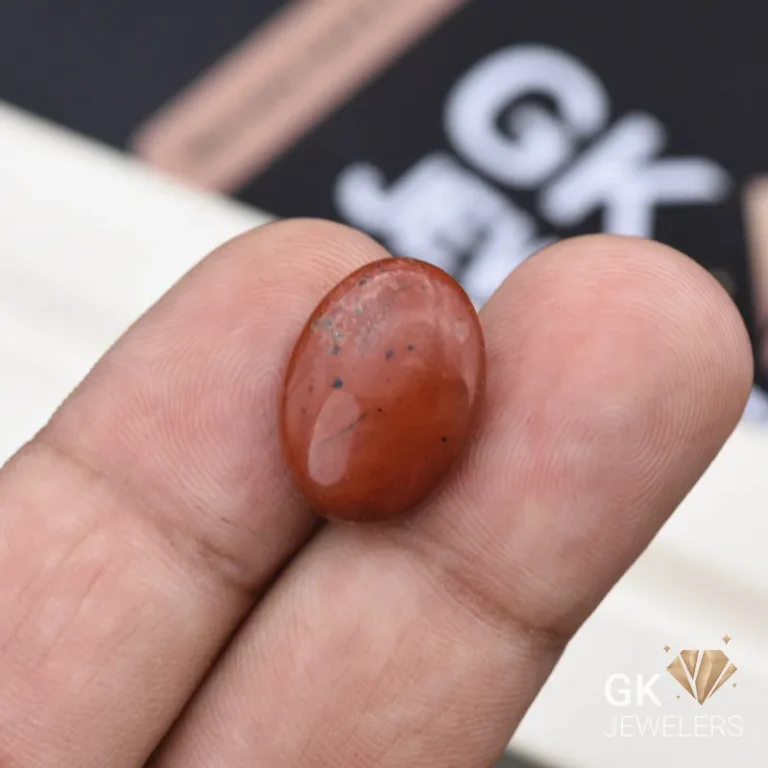 Oval red jasper gemstone held between person's thumb and fingers
