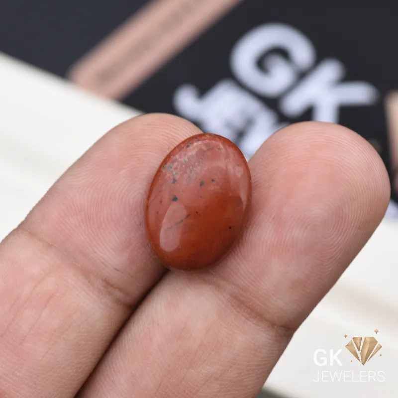 Oval red jasper gemstone held between person's thumb and fingers
