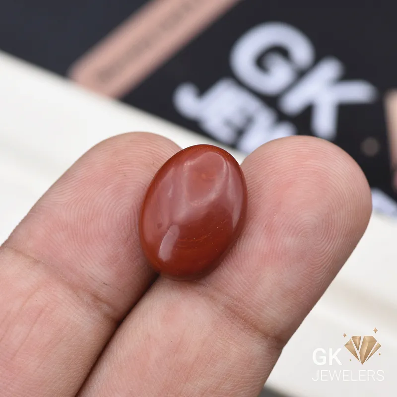 Oval red gemstone held between person's fingers with watermark logo