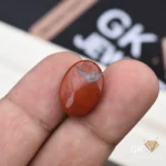 Red oval jasper gemstone held between person's thumb and finger
