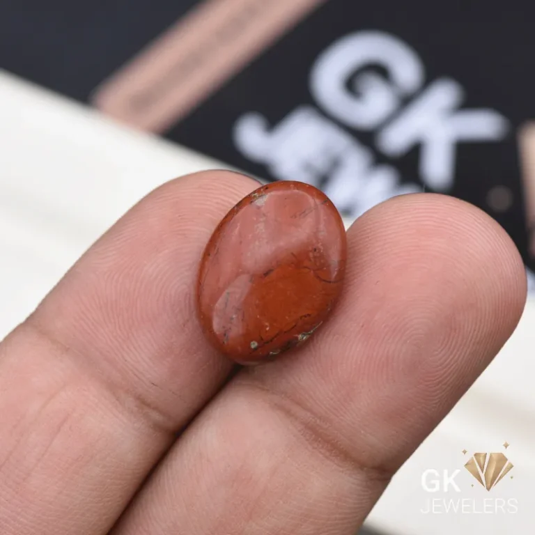 Oval red jasper gemstone held between person's thumb and finger