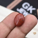 Oval red jasper gemstone with dark veins held between fingers