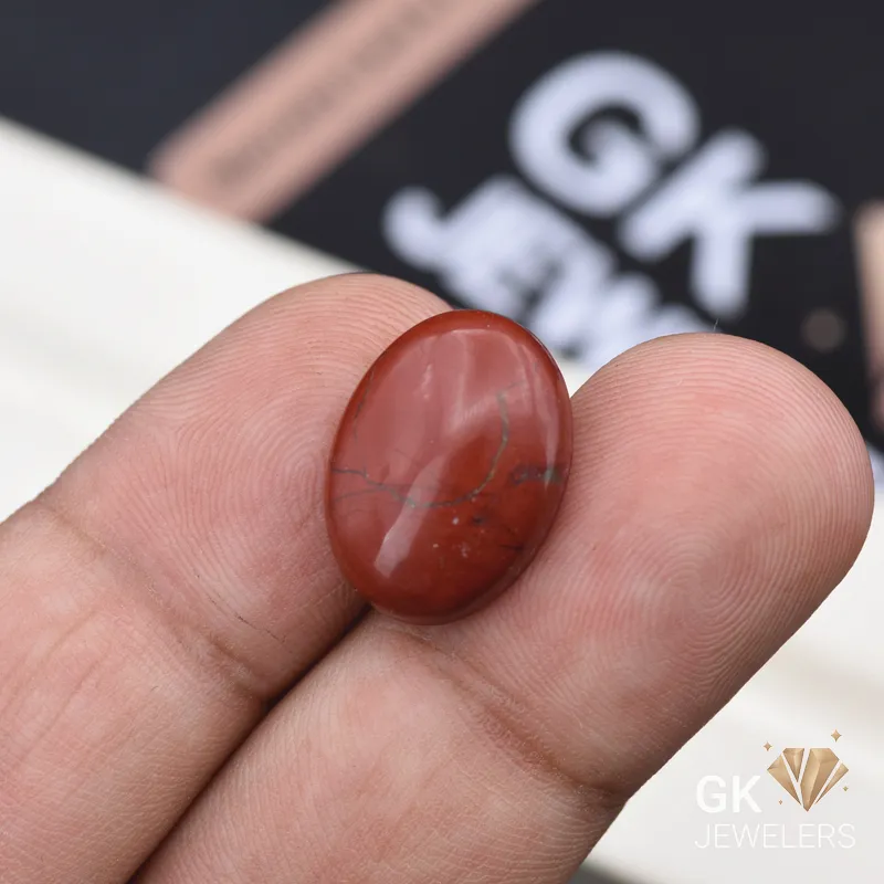 Oval red jasper gemstone with dark veins held between fingers