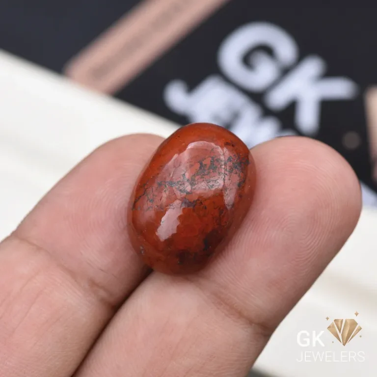 Polished red jasper gemstone with black inclusions held between fingers