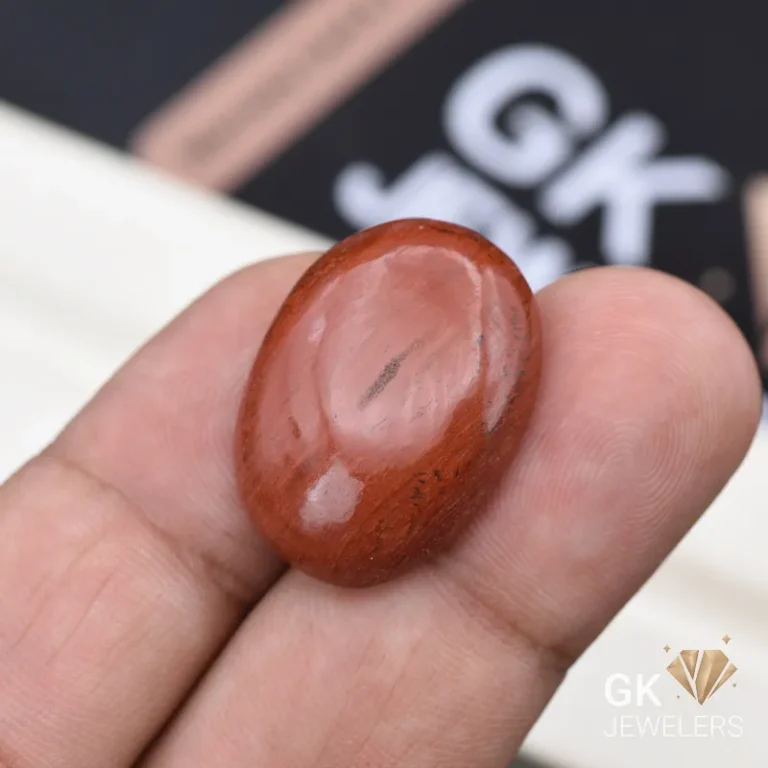 Oval red jasper gemstone held between person's fingers with watermark