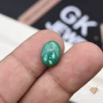 Oval green malachite gemstone held between person's index and middle fingers