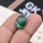 Oval malachite gemstone with green banded patterns held between fingers