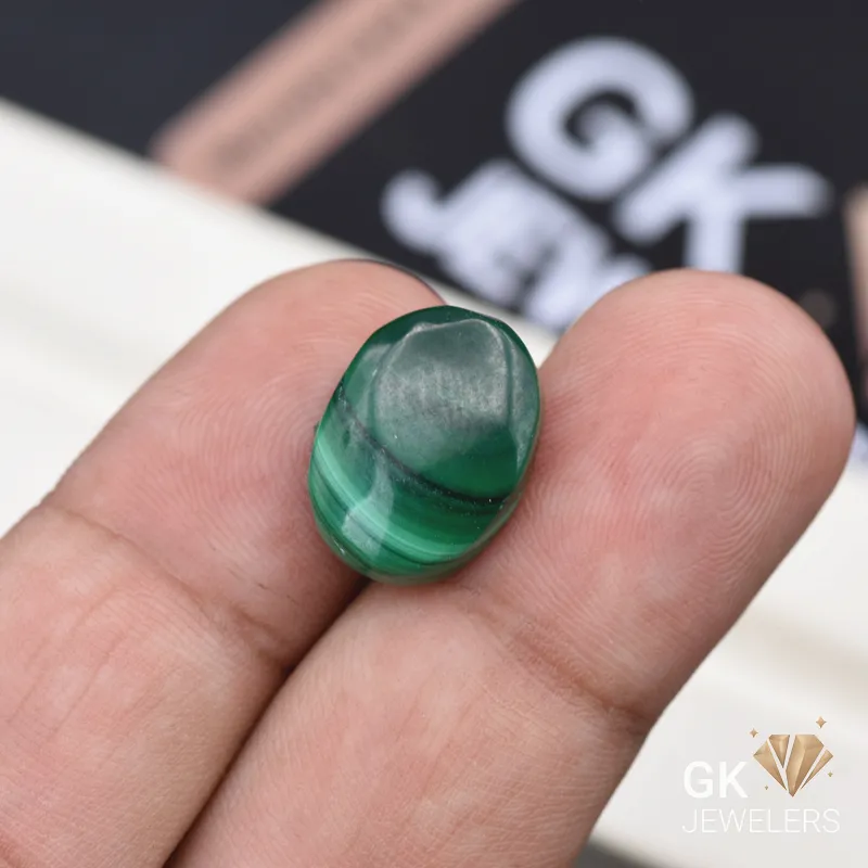 Oval malachite gemstone with green banded patterns held between fingers