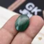 Oval polished malachite gemstone held between person's fingers with banded patterns