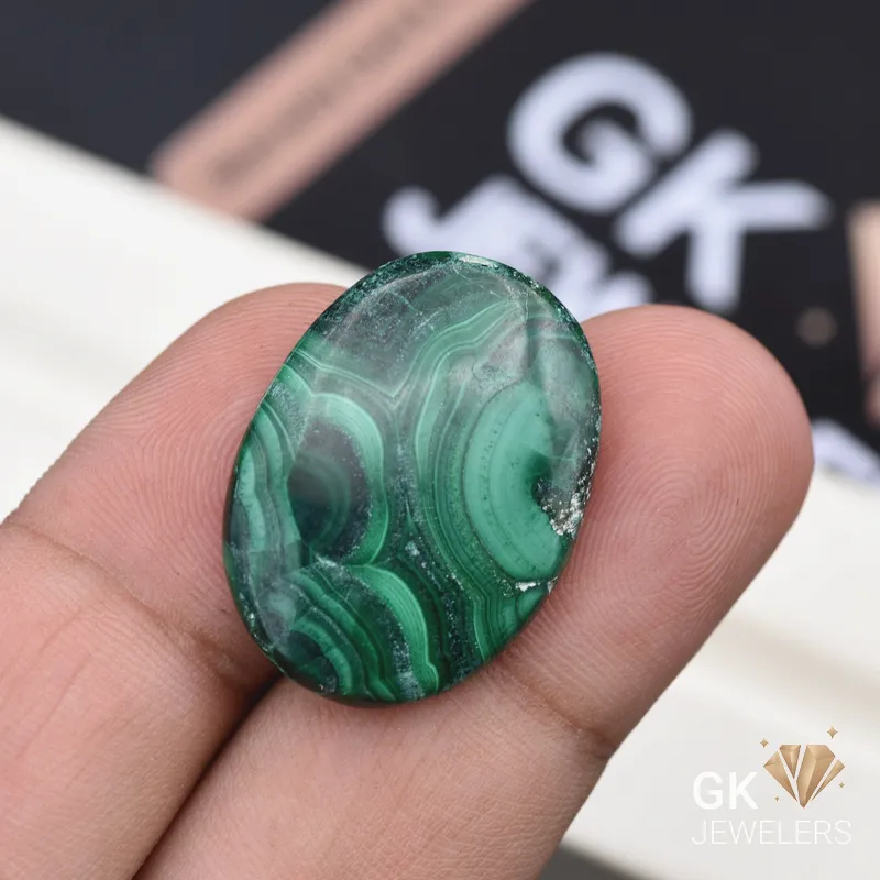 Fingertips holding polished oval malachite gemstone with banded patterns