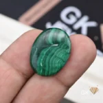 Oval cut polished malachite gemstone held between person's fingers