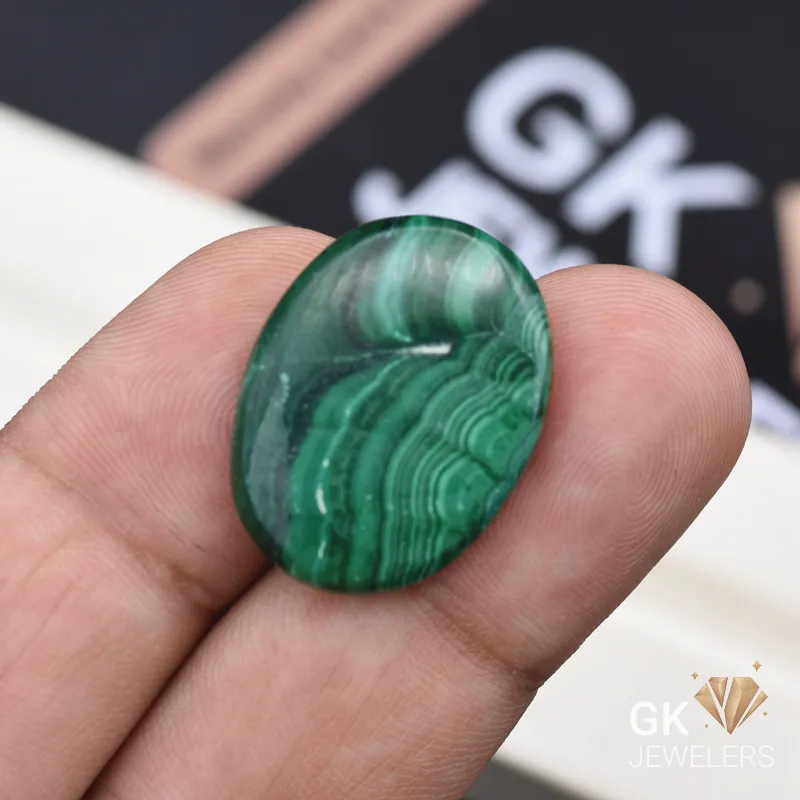 Oval cut polished malachite gemstone held between person's fingers