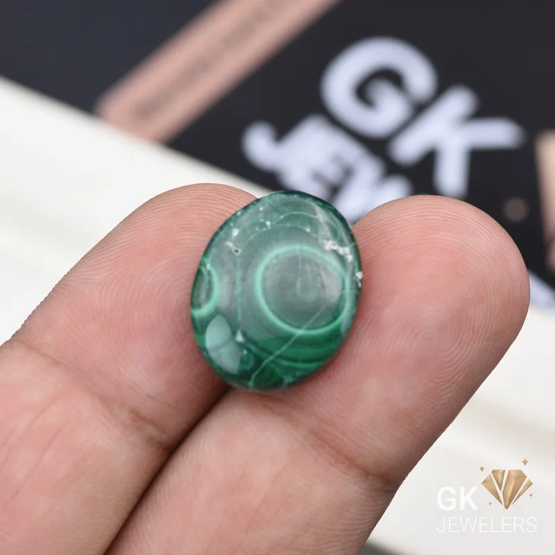 Oval-cut green malachite gemstone held between person's thumb and finger