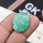 Oval-cut green malachite gemstone held between person's thumb and finger