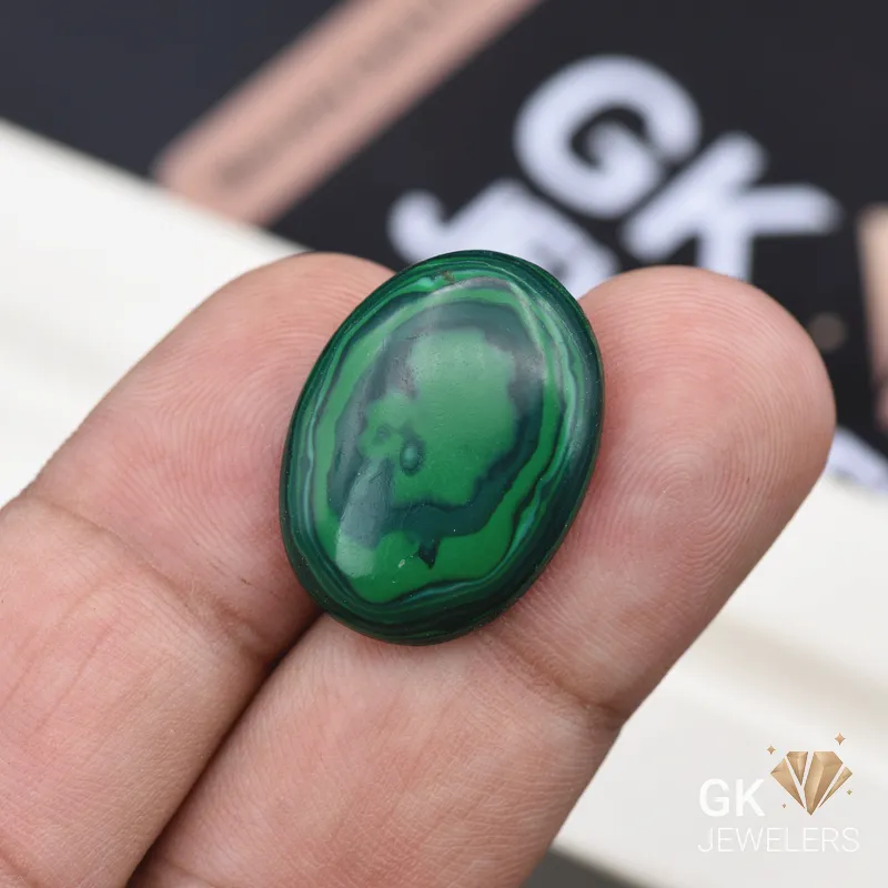 Oval-cut polished malachite gemstone held between person's thumb and finger
