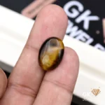 Oval tiger eye gemstone held between person's thumb and index finger