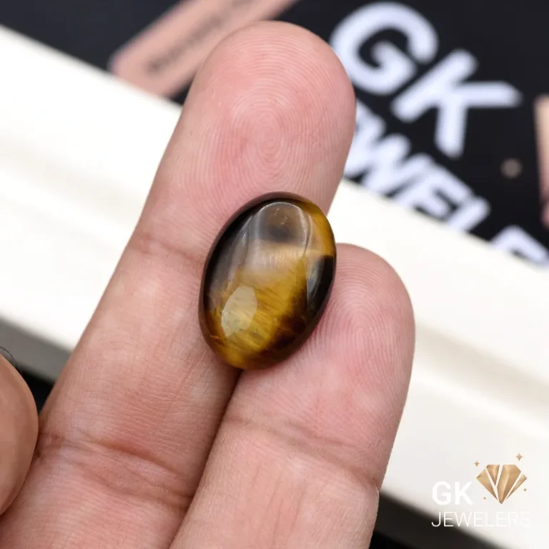 Oval tiger eye gemstone held between person's thumb and index finger