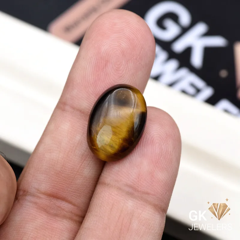 Oval tiger eye gemstone held between person's thumb and index finger