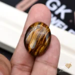 Oval tiger eye gemstone held between person's thumb and index finger
