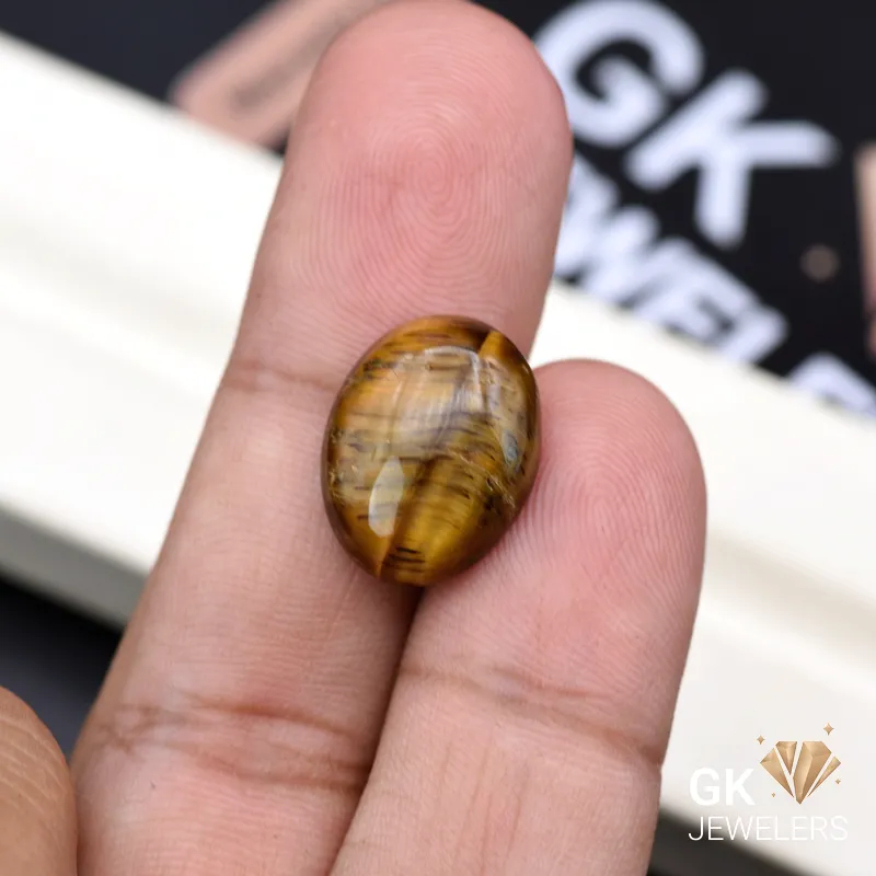 Oval tiger eye gemstone held between person's thumb and fingers