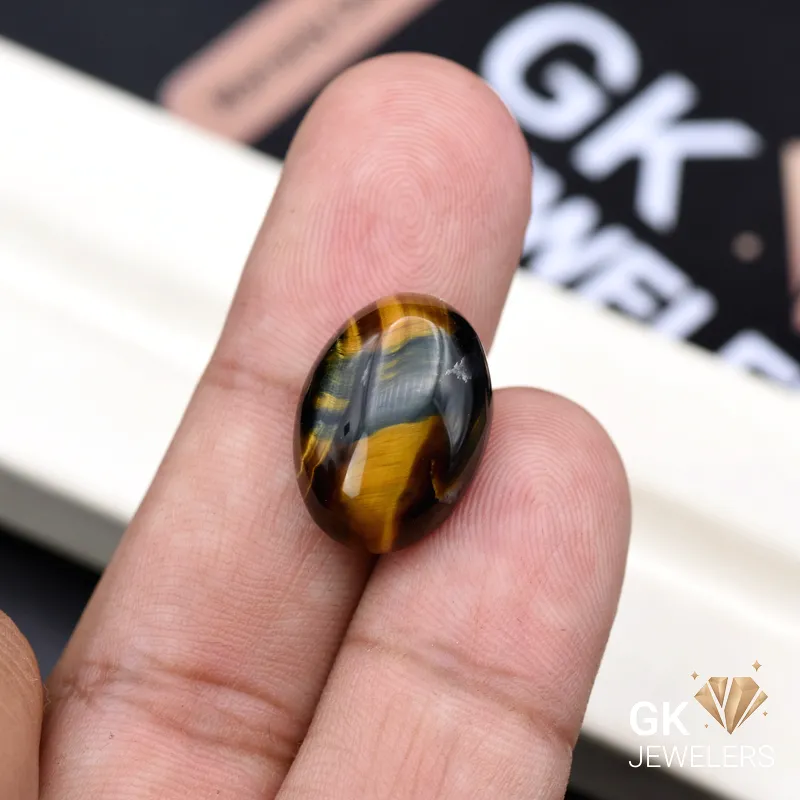 Oval Tiger Eye gemstone held between person's finger and thumb