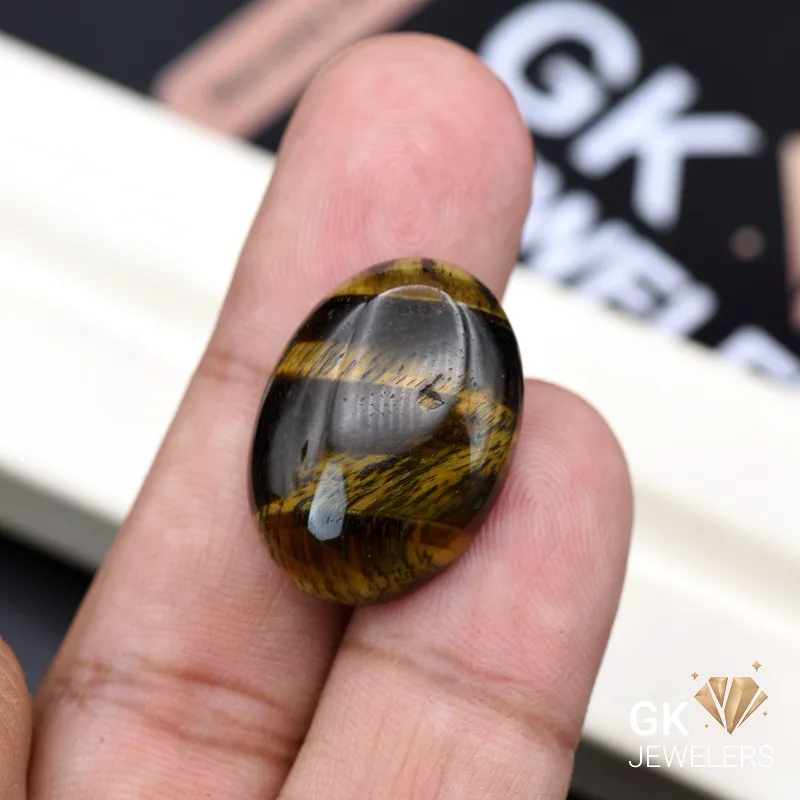 Oval Tiger Eye gemstone held between person's thumb and finger